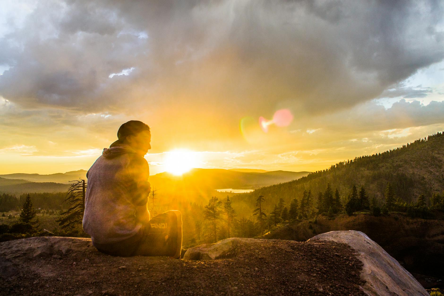 person sitting on stone facing sunset